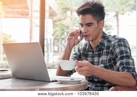 Businessman Using Mobile Phone While Lookingat Laptop On Wooden Table In Coffee Shop