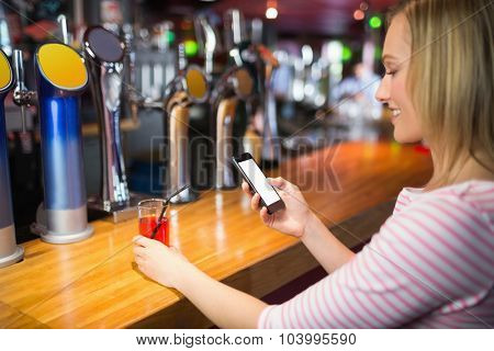 Young woman with mobile phone holding glass at bar counter