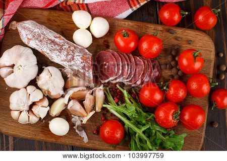 Salami With Cherry Tomatoes, Ruccola And Garlic On A Cutting Board