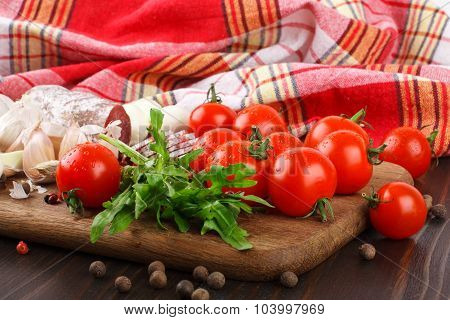 Cherry Tomatoes, Rucola, Spices, Garlic And Salami On A Cutting Board