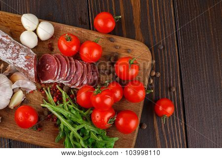 Salami With Cherry Tomatoes, Ruccola And Garlic On A Cutting Board