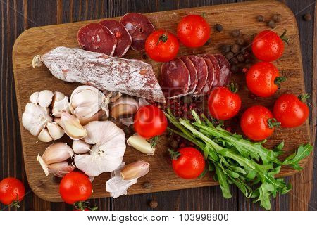 Salami With Cherry Tomatoes, Ruccola And Garlic On A Cutting Board