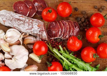 Salami with cherry tomatoes arugula and garlic on a cutting board. Close-up