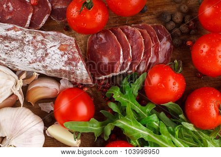Salami with cherry tomatoes arugula and garlic on a cutting board. Close-up