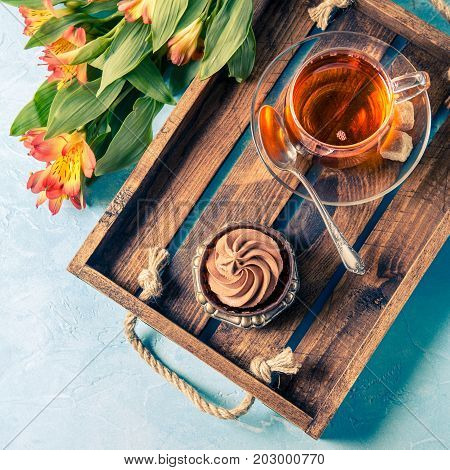 Image of light breakfast, black tea, cupkake with cream and orange flowers on wooden tray