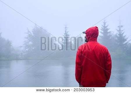 Back view of traveler in red waterproof jacket looking on the left near lake 