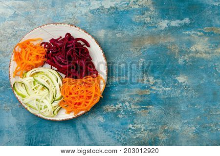 Zucchini carrot sweet potato and beetroot noodles on a plate. Top view overhead copy space. Blue rustic background