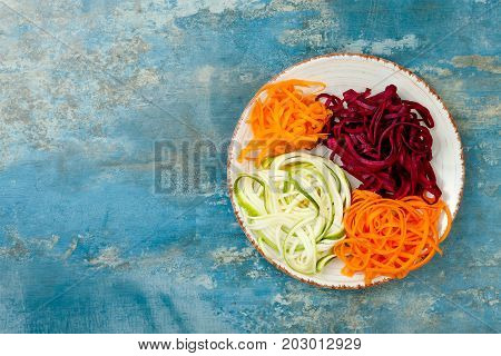 Zucchini carrot sweet potato and beetroot noodles on a plate. Top view overhead copy space. Blue rustic background