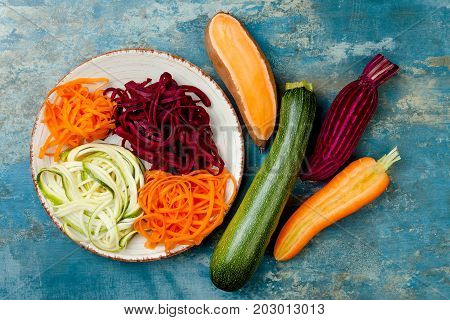 Zucchini carrot sweet potato and beetroot noodles on a plate. Top view overhead. Blue rustic background
