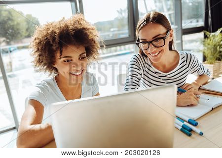 Modern students. Close up of joyful young students sitting at the table and enjoying distance learning while smiling
