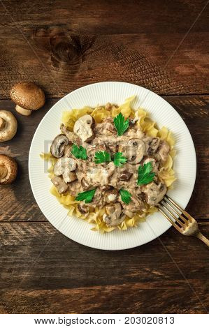 Mushroom beef stroganoff, served with the typical egg pasta, with cremini and champignons, with a fork, shot from above on a dark rustic texture with a place for text