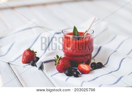 Smoothies of black currant and strawberries with yogurt on a white wooden table.