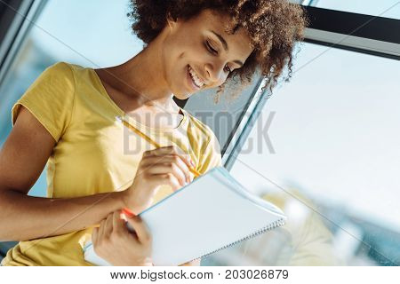 Put it down. Cheerful young curly afro american woman making notes in her notebook and smiling while feeeling happy
