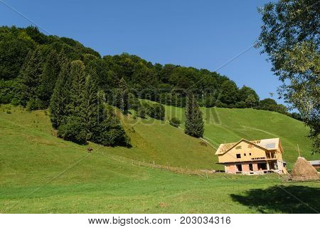 house under construction in the green hills covered with green forest and clear blue sky