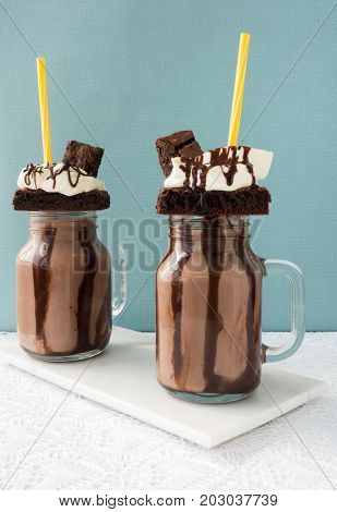 Two homemade Chocolate Freakshakes Milkshakes with brownies chocolate sauce and whipping cream.
