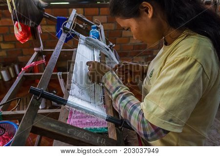 SIEM REAP CAMBODIA - AUGUST 24 2015: A girl weaves with silks at a silk farm.