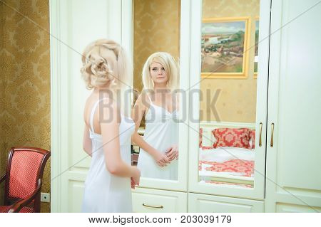 Morning of the bride. The blonde bride admires herself in the mirror.