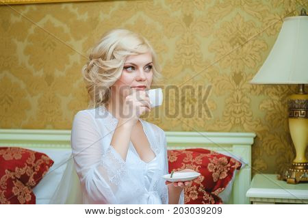 Morning of the bride. The blonde bride in the bedroom drinks coffee.