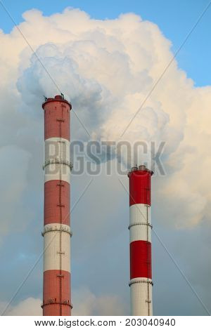 Two pipes of factory and white smoke in blue sky at sunny day