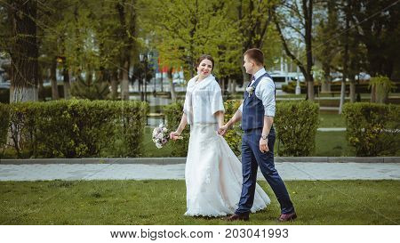 A happy couple of newlyweds strolls on the lawn.