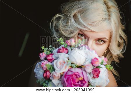 charming blonde girl with a bouquet of flowers on a dark background.