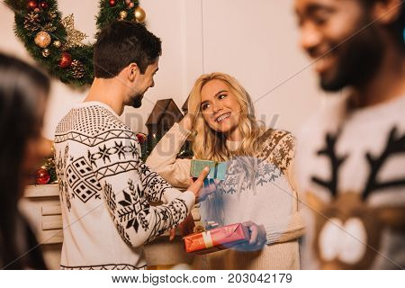 selective focus of multiethnic couple exchanging christmas gifts during christmas celebration