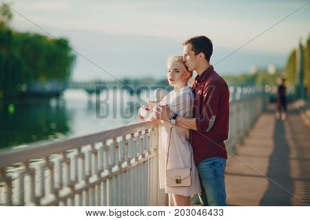A beautiful blonde in a pink dress with her handsome guy in a red shirt is good at spending time near river