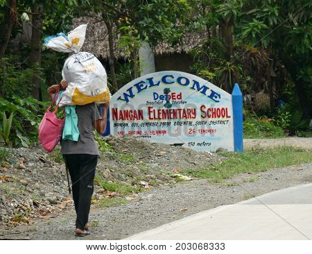 DAVAO ORIENTAL, PHILIPPINES--MARCH 2016: A man walks along the street carrying a big sack and bag along the road of Banay Banay, Davao Oriental, southern Philippines.