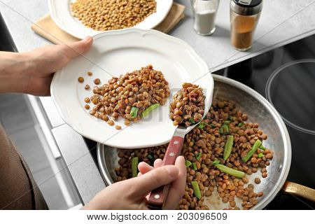 Chef putting tasty lentils onto plate in kitchen
