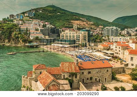Budva, Montenegro - August 20, 2017: Fragment of the old town of Budva: ancient walls and a red tiled roof and a view of a modern beach, Montenegro, Europe. Budva is one of the best and most popular resorts of the Adriatic Riviera.