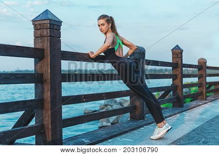 Beautiful Brunette Sporty Caucasian Female Woman Stratching Outdoors. Fit Woman Near Lake. Fitness M
