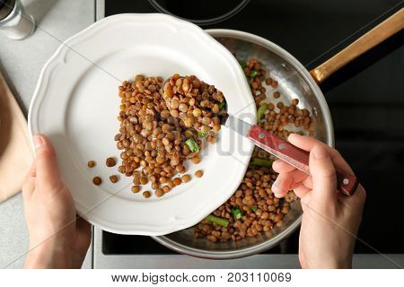 Chef putting tasty lentils onto plate in kitchen