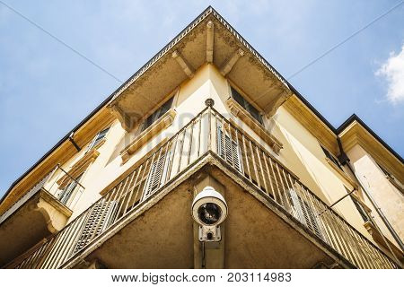 An old yellow house facade with a surveillance camera below the balcony in a sunny day with blue sky and clouds.