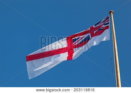 Royal navy ensign flying in the wind on a sunny day with a blue sky and space for text.
