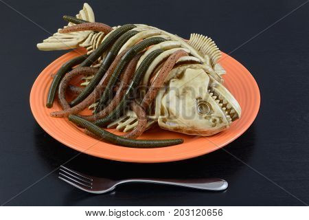 Halloween dinner dish worms crawling out of fish skeleton on orange plate with fork on black table