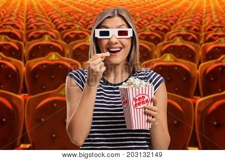 Young woman wearing 3D glasses and eating popcorn at the cinema