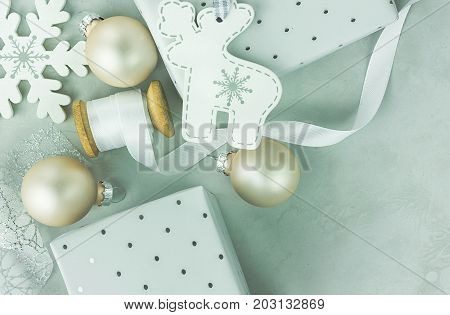 Gift boxes wrapped in silver paper with polka dots pattern. Wooden spool with white curled silk ribbon Christmas baubles reindeer fir tree ornament on stone marble background. Top view copy space.