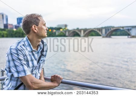 Young man looking over potomac river with Francis Scott Key Bridge during sunset