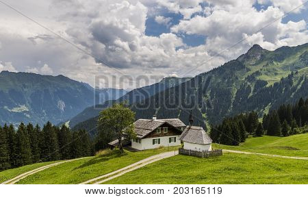 Old wooden cabin and chapel in Matschwitz with in the background the mountains of Montafon on a summers day Austria