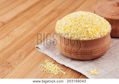 Corn grits in wooden bowl on brown bamboo board closeup. Rustic style healthy dietary groats background.