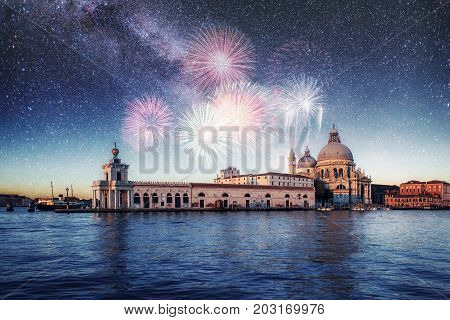 Night illumination of buildings and boats near the water. Venice. Photo greeting card. Colorful fireworks on the black sky background