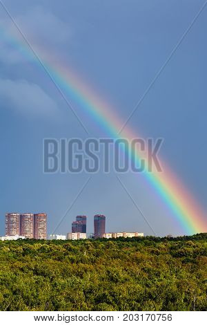 Rainbow In Dark Blue Sky Over City And Urban Park
