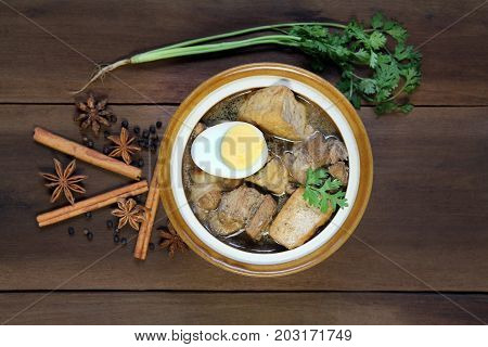 Belly Pork Chinese Five-Spice Stew with boiled egg and fried tofu braised in brown sauce decorated with anise star black pepper cinnamon and coriander on wooden background, Asia food.