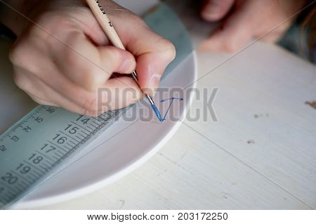 The artist paints an anchor on a white plate made of clay. Painted, handmade