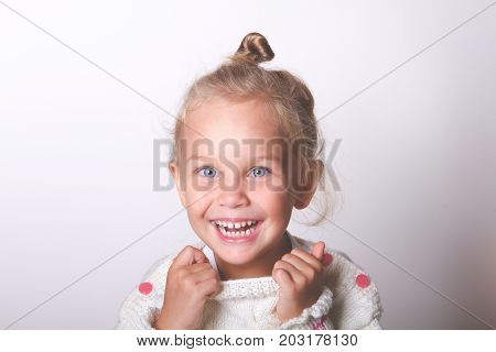 Portrait of a beautiful liitle girl close-up. looks at the frame blue eyes in a light knitted sweater laughs and smiles. film toned