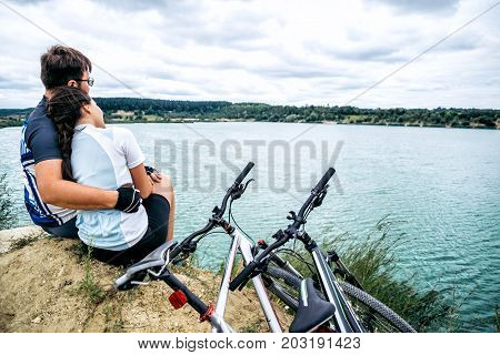 couple sits and looking at the lake two bicycles near them zure water on background
