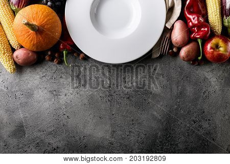 Seasonal Harvest Autumn Concept. Empty Plate with Tasty appetizing fresh autumn seasonal vegetables fruits on grey background top view above copy space