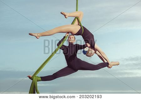 Two women aerial gymnasts perform high in the sky on hammocks.