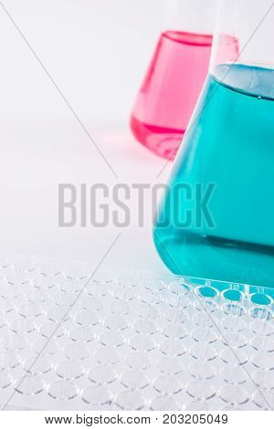 research, science and clinic background. 96 well micro plate and  laboratory beakers with colorful liquids and reagents.