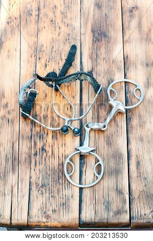 Steel horse snaffle-bit and spurs on wooden background. Outdoors vertical close-up image.